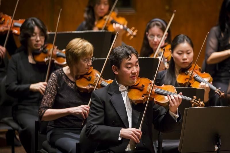 Violiste in rokkostuum speelt vooraan tussen orkestmusici
