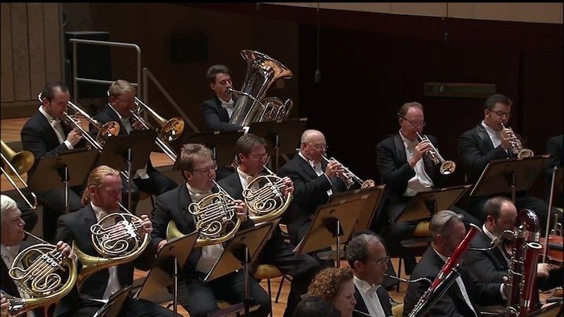 Koperblazers spelen naast houtblazers in een orkest op het podium