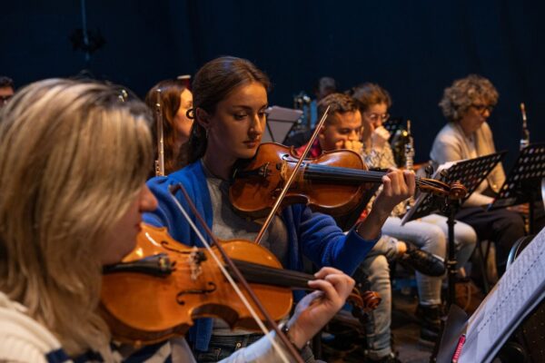Strijkers repeteren samen, met een violiste prominent op de voorgrond